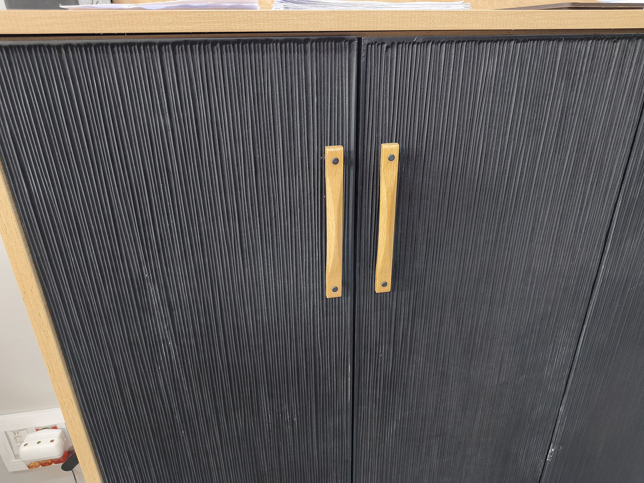 Mueble de madera con puertas texturizadas fabricadas mediante mecanizado CNC, acabado en negro y tiradores de madera natural.