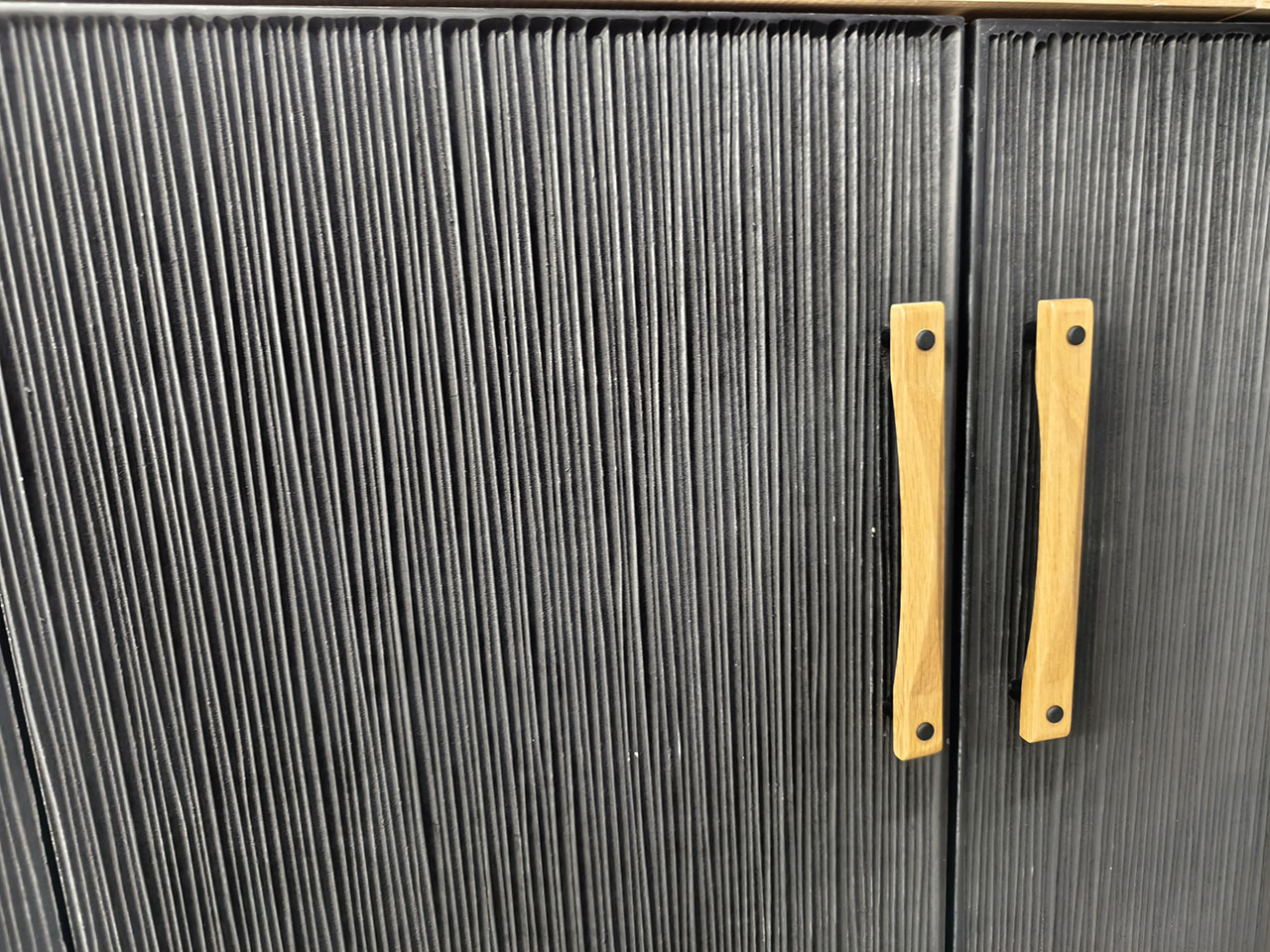 Mueble de madera con puertas texturizadas fabricadas mediante mecanizado CNC, acabado en negro y tiradores de madera natural.
